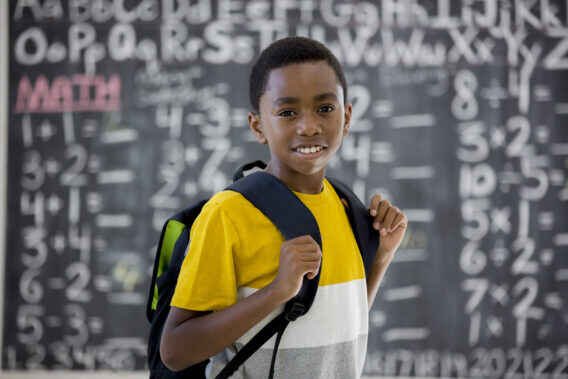 elementary school boy smiling while standing in front of the chalkboard